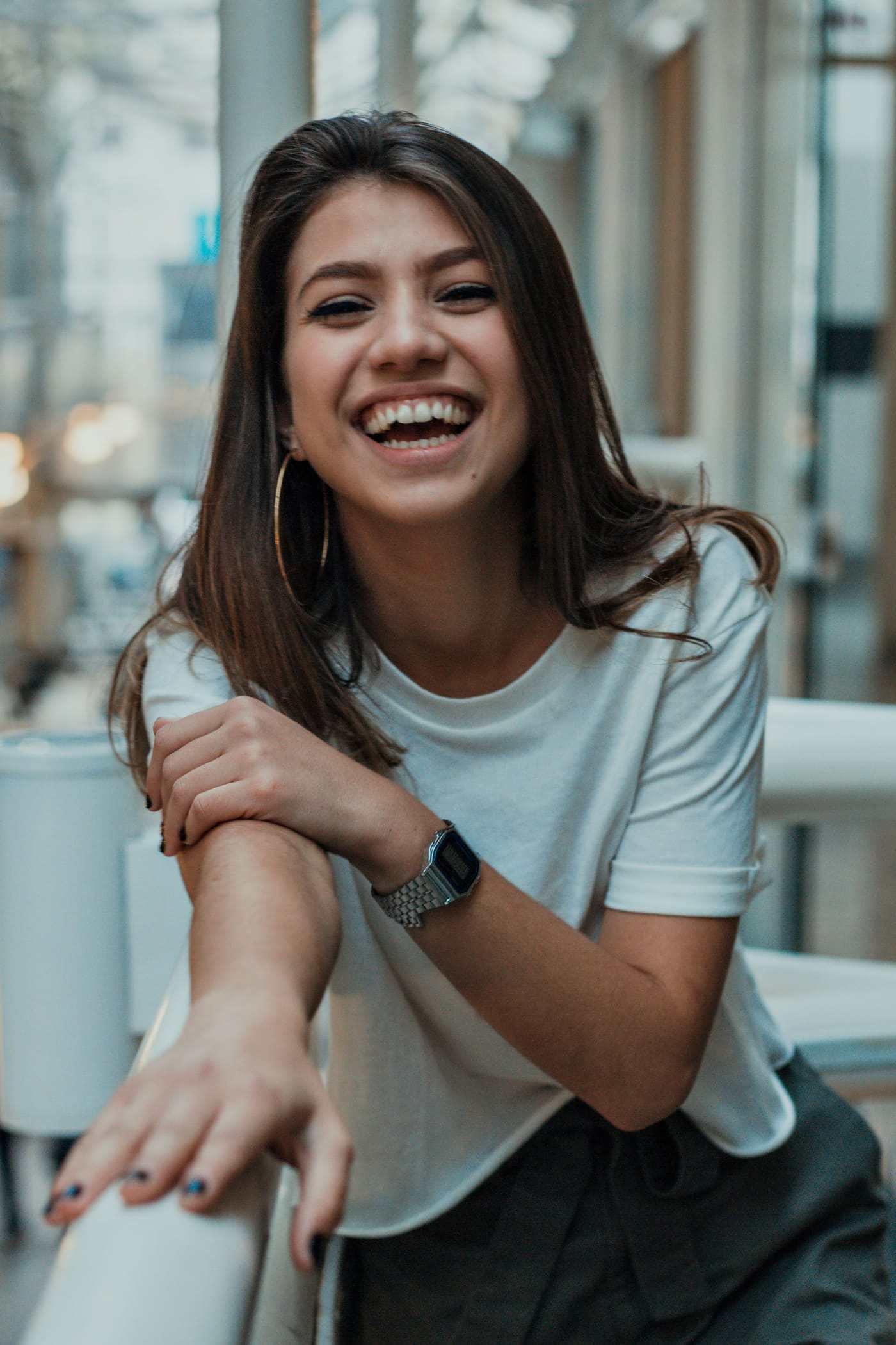 A laughing woman in a white t-shirt leaning on a railing, photographed on a city street