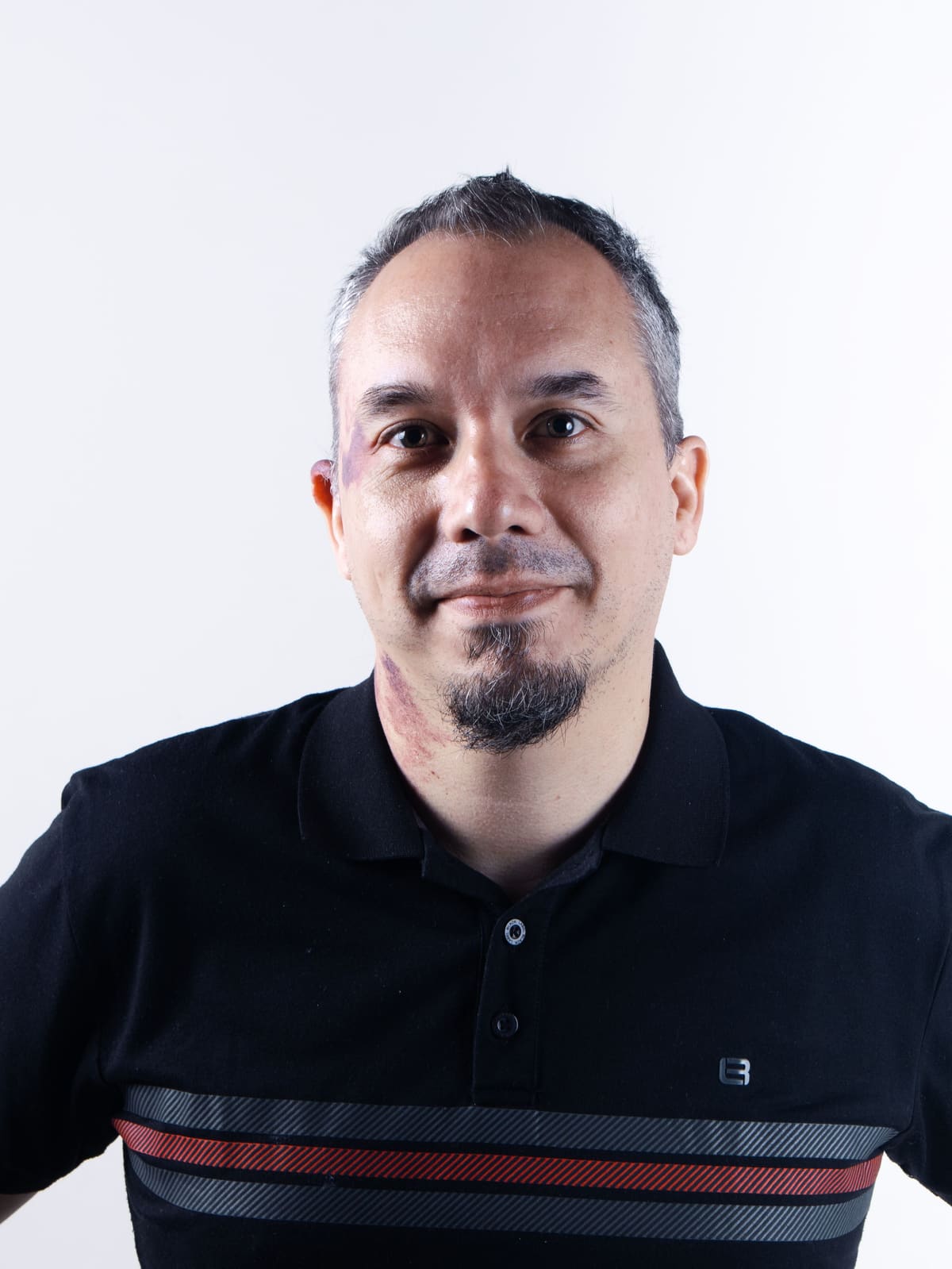 A relaxed portrait of a man in a black polo shirt photographed against a plain white background