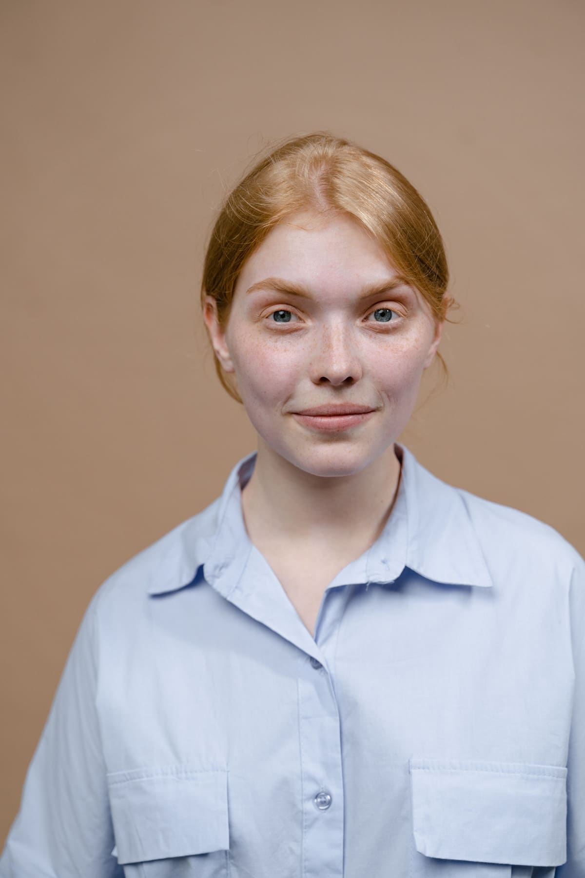 Studio headshot of a woman with red hair in a pale blue shirt against a warm beige backdrop