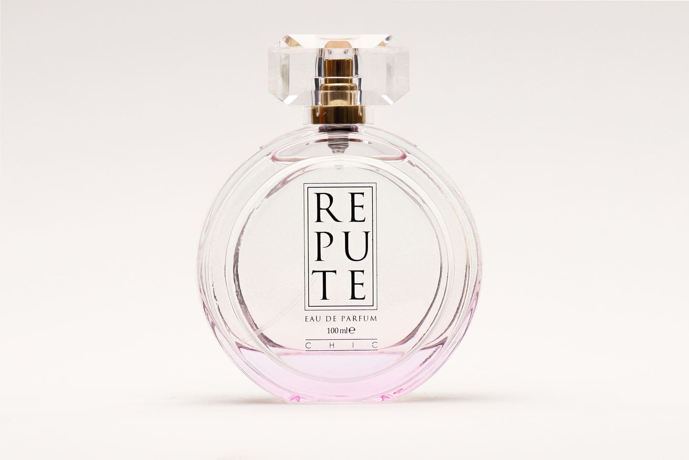 A round glass perfume bottle photographed against a plain pale background