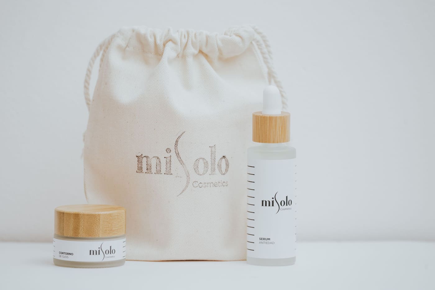 Skincare bottles and a cotton drawstring pouch photographed on a white surface