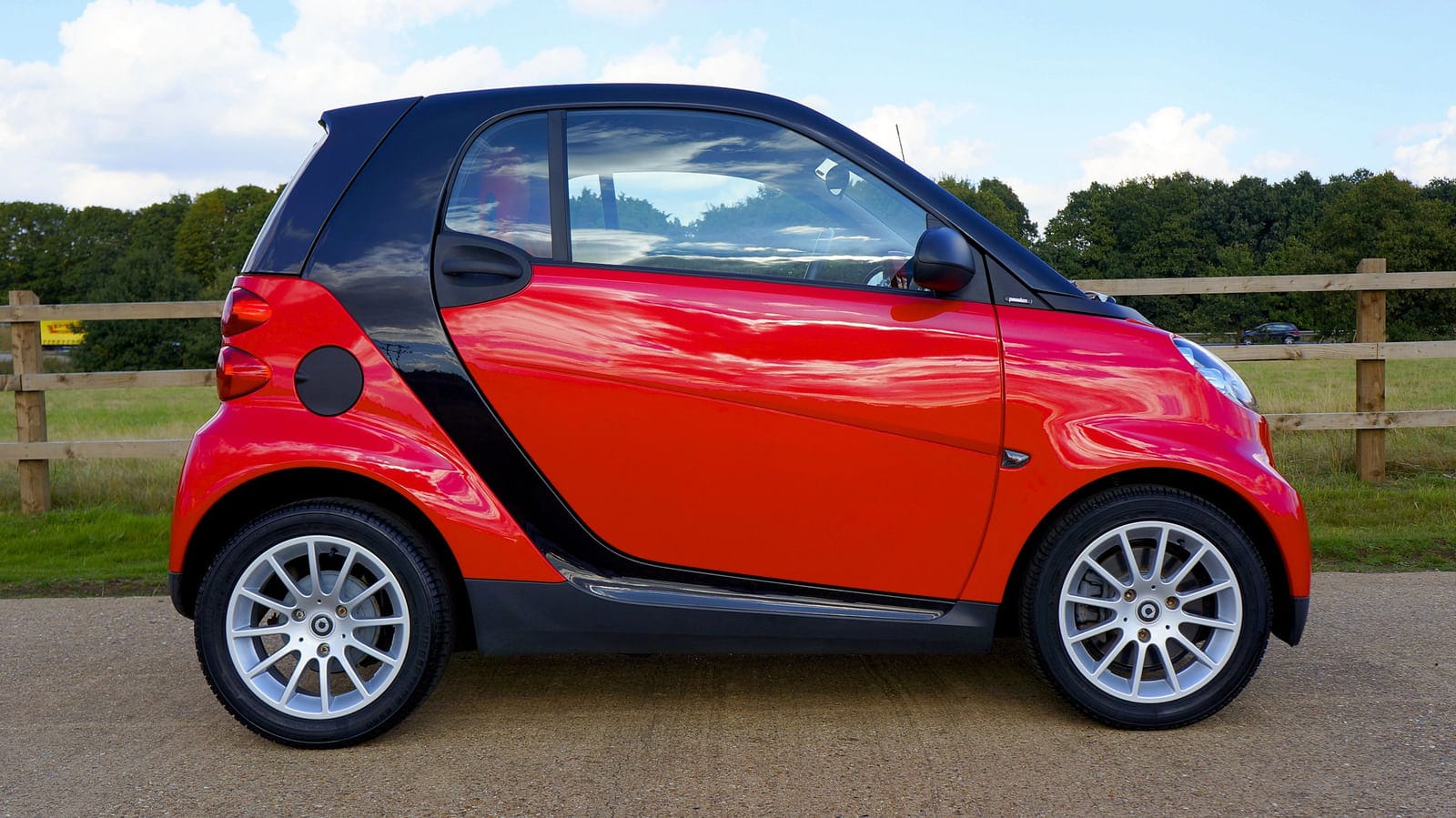 A red and black Smart ForTwo photographed in side profile on a road.